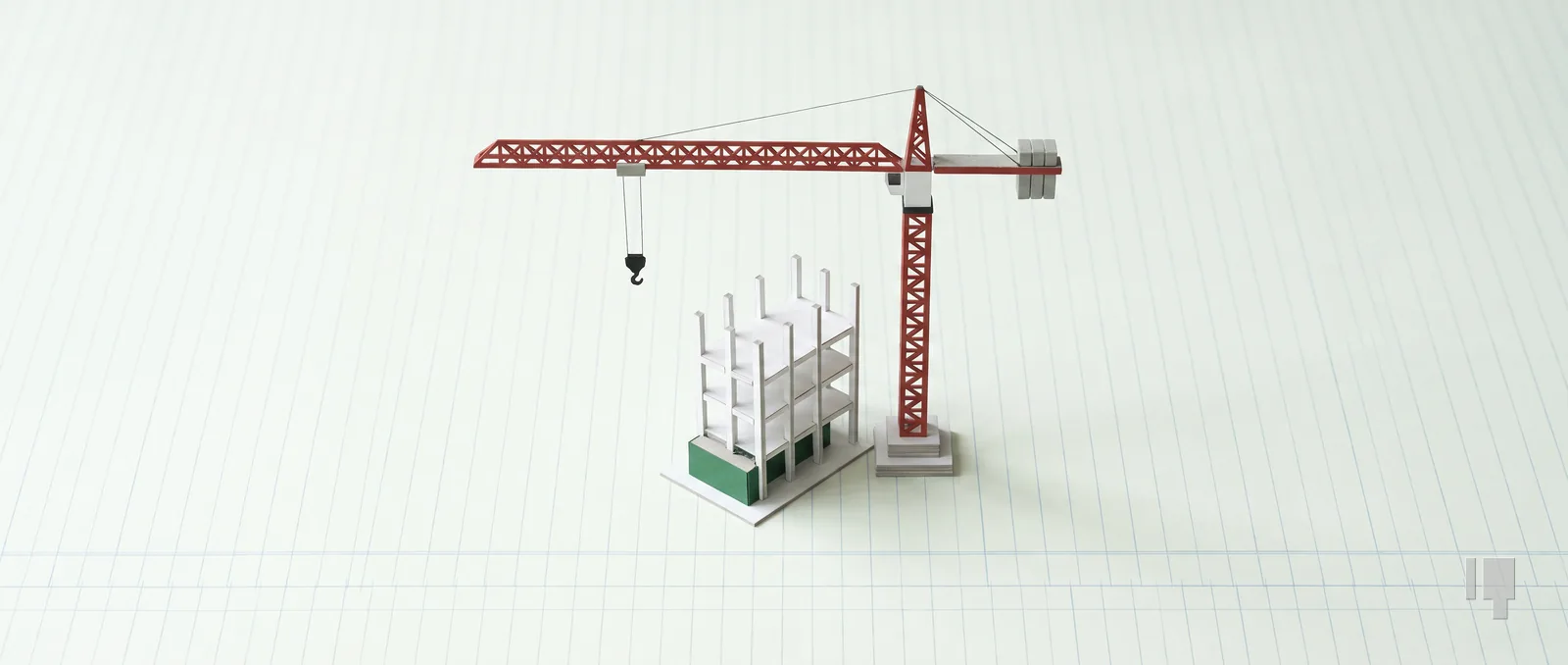 Scale model of a tower crane with a red jib beside a card model of a building frame, on a green ledger pad